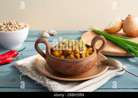 Geschmorte Kichererbsen mit Zwiebeln und Curry in einer Keramikschale auf Holzgrund. Rustikaler Stil. Vegetarisches Essen. Gesunde Ernährung Stockfoto