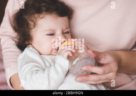 Kleine Mädchen versuchen, Trinkwasser aus Plastikflasche in den Händen der Mutter zu trinken. Kindheit. Mutterschaft. Stockfoto