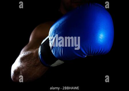 Die Hand der Männer in einem blauen Boxhandschuh auf schwarzem Hintergrund macht einen Schlag Stockfoto