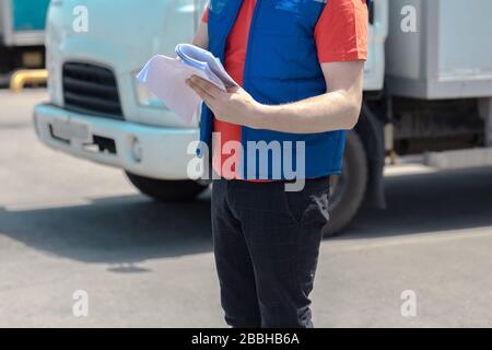 Kurierfahrer in Uniform macht Notizen in Dokument und Lieferung weißer LKW behinde ihn Stockfoto