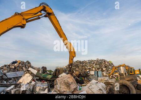 Ein Kran bewegt Metallteile durch Berge von Altmetall in einem Schrottplatz Stockfoto