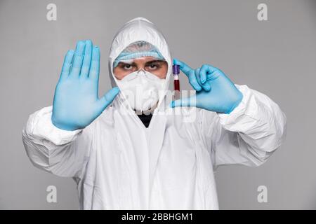 Der Mann Doktor in der Schutzkleidung hält einen Reagenzglas mit einer Probe infiziertem Blut in der Hand und zeigt Stoppzeichen von einer anderen Hand. Stockfoto