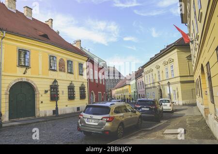 Budapest, Ungarn - 6. November 2019: Schöne historische Straße mit bunten Häusern im historischen Zentrum. Geparkte Autos auf der gepflasterten Straße. Altstadt der ungarischen Hauptstadt. Horizontales Foto. Stockfoto