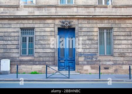 Hohe blaue Holztür mit zwei schmalen Fenstern an der grauen Gebäudefassade, Bordeaux, Frankreich Stockfoto