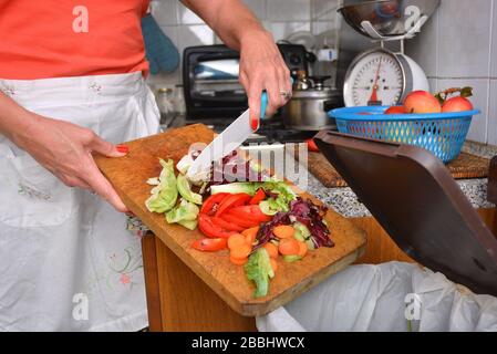 Detail einer weiblichen Hand Entsorgung der organischen Abfälle in einem geeigneten Behälter mit Küche im Hintergrund Stockfoto