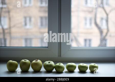 Eine Reihe grüner Äpfel liegt auf einem steinernen Fensterbrett am Fenster. Kopierbereich. Stockfoto