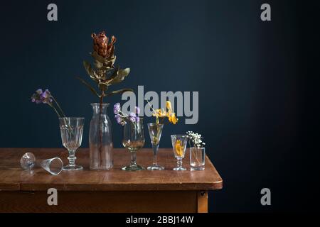 Getrocknete Blumen in Glasgläsern auf einem Holztisch gegenüber einer dunkelblauen Wand. Kunstkarte. Design. Kopierbereich. Stockfoto