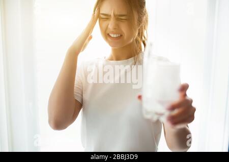 Junge Frau während der Quarantäne im Zimmer. Schnittansicht oder weibliche Person leidet unter Kopfschmerzen. Halten Sie ein Glas Wasser mit einer Brausetablette darin. Hilfe bei Stockfoto