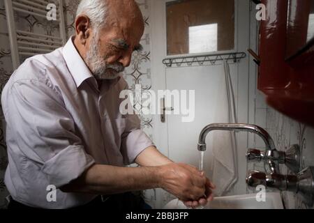 Sehr alter türkischer Mann, der seine Hände in seinem alten Badezimmer wascht, um ihn vor Coronavirus zu schützen Stockfoto
