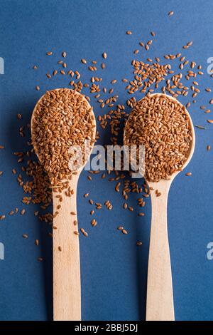 Flach legen Sie zwei Holzlöffel mit braunen Flachssamen auf blauem Grund. Stockfoto
