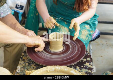 Die Hände eines Meisters und eines Studenten machen einen Krug aus gelbem Ton Stockfoto