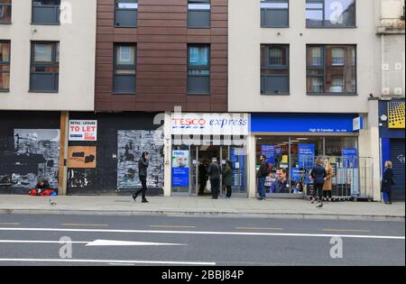 Soziale Isolierung von Warteschlangen außerhalb von Supermärkten in der Coronavirus Pandemie an der Camden High Street in London, Großbritannien Stockfoto