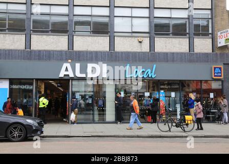 Soziale Isolierung von Warteschlangen außerhalb von Supermärkten in der Coronavirus Pandemie an der Camden High Street in London, Großbritannien Stockfoto