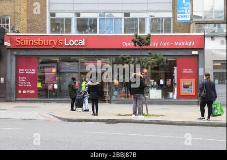 Soziale Isolierung von Warteschlangen außerhalb von Supermärkten in der Coronavirus Pandemie an der Camden High Street in London, Großbritannien Stockfoto