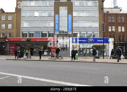 Soziale Isolierung von Warteschlangen außerhalb von Supermärkten in der Coronavirus Pandemie an der Camden High Street in London, Großbritannien Stockfoto