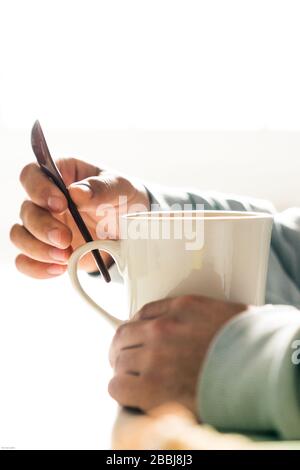 Person, die einen Löffel hält, um eine Tasse Kaffee zu trinken Stockfoto