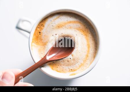 Cremige Kaffeetasse mit einem Finger, der einen Keramiklöffel hält. Zenithale Ansicht. Stockfoto