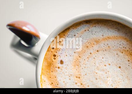 Zenithaler Blick auf eine sehr cremige Kaffeetasse mit Keramiklöffel Stockfoto