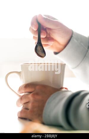 Person, die eine weiße Kaffeetasse mit einem Keramiklöffel mischt. Stockfoto