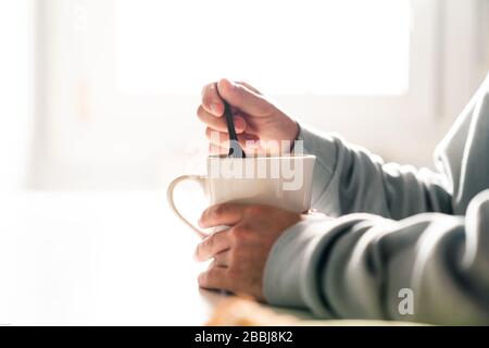 Person, die eine Kaffeetasse mit einem Keramiklöffel mischt. Die Hände einer Person. Stockfoto