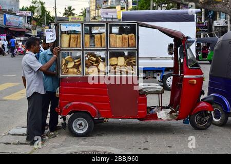 Weligama, Sri Lanka - April 2017: Mann verkauft Brot aus seinem roten Dreiradfahrzeug (Tuk Tuk) auf dem Straßenmarkt Stockfoto