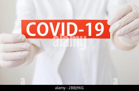 COVID-19 Coronavirus, rotes Warnschild mit Text COVID-19 in den Händen des Arztes in weißem Mantel, Handschuhe, Gesichtsmaske.Quarantäne Coronavirus Epidemie Stockfoto