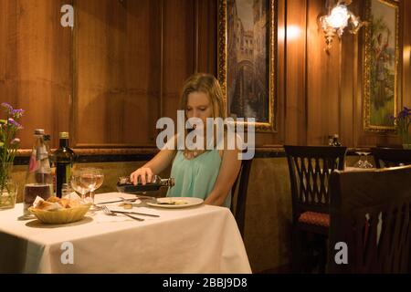 Frau gießt Essig auf einen Teller in einem Restaurant mit Holzvertäfelung und Leinentischdecken in der Nähe der Rialto-Brücke, Venedig, Italien Stockfoto