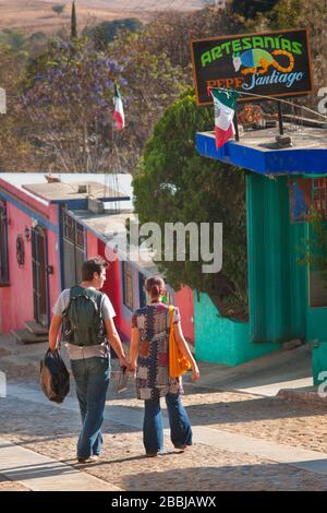 Ein Paar geht zu einem Geschäft in dieser kleinen Gemeinschaft von Handwerkern, die bunte Kopal Alebrijes, bemalte Holztiere, in Arrazola, Valles Centrales zu schaffen Stockfoto