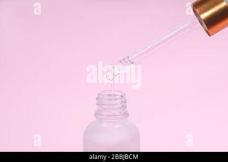 Einfüllstck aus Tropfglas. Öliger Tropfen fällt von der kosmetischen Pipette auf rosa Hintergrund. Hautpflegekonzept. Stockfoto