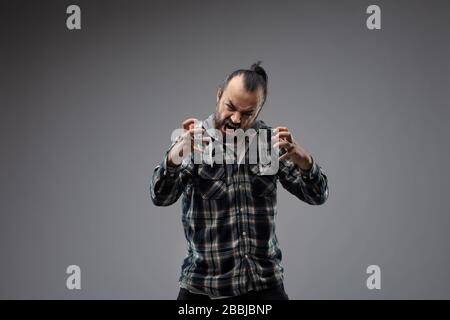 Bärtiger Mann mit gekämmtem schwarzem Haar, kariertem Hemd, aggressivem Grimace und Gesten mit den Händen nach oben drücken. Vorderer Anschluss mit halber Länge Stockfoto