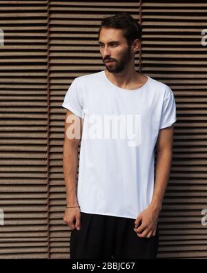 Ein bärtiger Hüpfer in einem weißen T-Shirt, das gegen eine rostige Metallwand posiert. Stockfoto