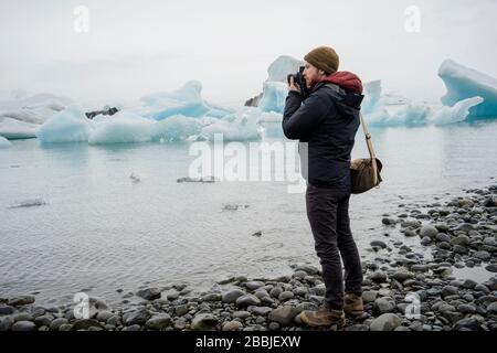 Mann, der in der Dämmerung ein Foto an der Gletscherlagune Jokulsarlon gemacht hat Stockfoto