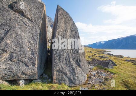 Backpacker quetscht sich durch Split in riesigen geknackten Boulder. Stockfoto