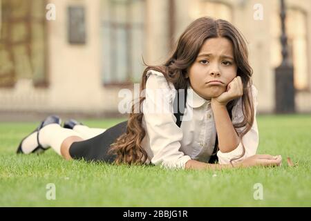 Traurig ohne ein Lächeln. Traurig Schulmädchen auf grünem Gras entspannen. Adorable kleine Kind mit traurigen Emotionen im Gesicht. Traurig und unglücklich. Traurigkeit und Depression. Schule Probleme. Stockfoto