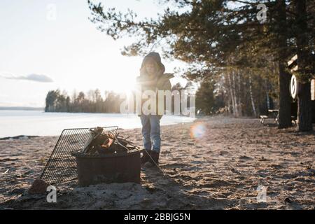 Der Junge stand neben einem Feuer am Strand in Schweden Stockfoto