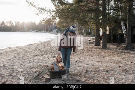 Frau, die im Winter einen Wasserkocher auf einem Kamin am Strand stellt Stockfoto