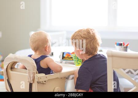 Rückansicht Baby Mädchen und junger Bruder, der Telefon am Tisch drinnen sieht Stockfoto