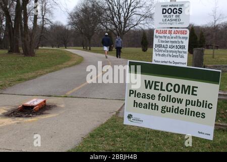 Willkommen, bitte folgen Sie den Richtlinien für die öffentliche Gesundheit in Skokie, Illinois' Harms Woods mit zwei Wanderern im Hintergrund während der COVID-19-Sperre Stockfoto