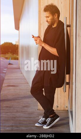 Ein Mann in einem modischen schwarzen Outfit, der bei Sonnenuntergang eines warmen Sommertags in Sportschuhen posiert. Streetstyle. Stockfoto