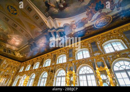 Ein prunkvoller goldener Festsaal im Inneren mit einer farbenfrohen bemalten Decke im Festsaal des Rokoko-Katharinenpalasts in Puschkin bei Sankt Petersburg, Russland. Stockfoto