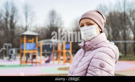 Frau auf dem Spielplatz mit einer chirurgischen Maske im Gesicht während der Coronavirus-Pandemie COVID-19. Menschen, die wegen einer Coronavirus-Krankheit eine medizinische Maske auf der Straße tragen. Stockfoto