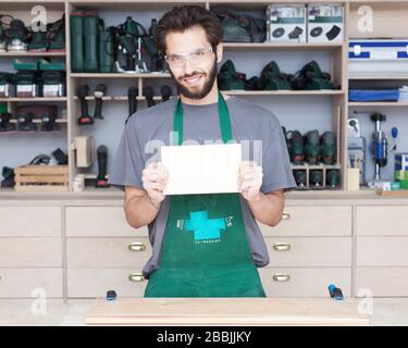 Ein Tischler, ein junger bärtiger Flusspferd in einer Zimmerei, hält ein Schild in der Hand, ein Banner. Stockfoto