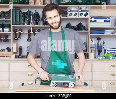 Ein gelernter Zimmermann verwendet den Stromschleifer als Werkzeug, um seine Möbel zu polieren. Workshop. Stockfoto