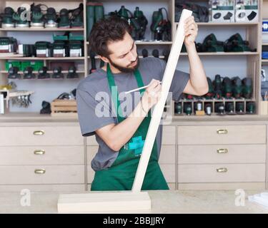 Der Tischler bärtige Reißverschluss in Arbeitskleidung arbeitet in der Werkstatt mit Holzdetails. Stockfoto