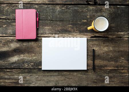 Draufsicht auf das digitale Tablett in pinkfarbener Abdeckung, leeres weißes Blatt Papier, schwarzer Stift und eine Tasse frischen Kaffee auf einem rustikalen Holzschreibtisch. Stockfoto