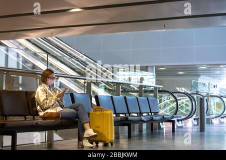 Frau verärgert über die Flugannullierung, schreibt Nachricht an Familie, sitzt in fast leerem Flughafenterminal wegen Coronavirus-Pandemie/Covid-19-Ausbruch Stockfoto