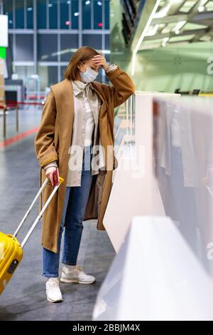 Frau mit Gepäck wegen Stornierung des Flugs verärgert, steht an leeren Check-in-Schaltern am Flughafenterminal wegen Coronavirus-Pandemie/Covid-19-Outb Stockfoto