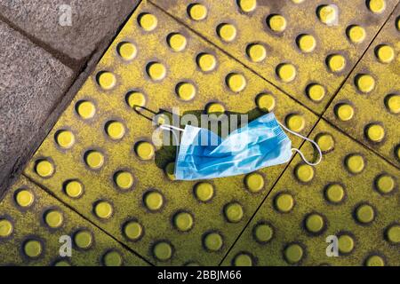 Blau schmutzig verwendete chirurgische Gesichtsmaske zum Schutz von Coronavirus auf gelben taktilen Pflastersteinen. Entsorgung medizinischer Abfälle. Draufsicht. Allergiesaison, Staubluft. Stockfoto