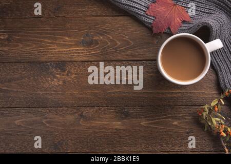 Flatlay-Komposition mit Strickschal, Tasse Kaffee und gelben Blättern auf Holztisch. Hygge-Stil, gemütliches Herbst- oder Winterferienkonzept. Flach Stockfoto