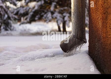 Drainpipe an der Ecke des Hauses mit Eis bedeckt, verschneiten Garten Stockfoto